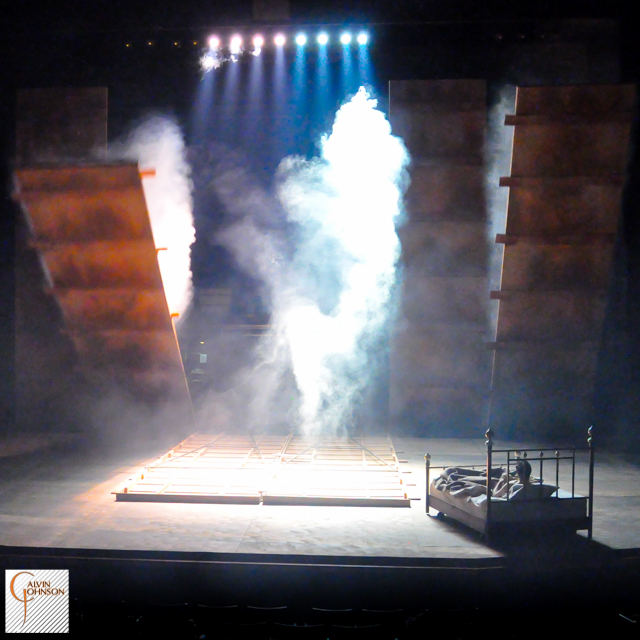 "Angels In America" at Carnegie Mellon. Beams of bright light shine down on Prior Walter while laying in bed as the wall falls around him.