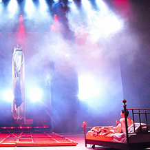 "Angels In America" Bright red and white beams of light shine down on Prior Walter lying in bed after the wall has fallen and the Angel decends.