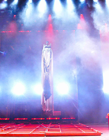 Bright red and white beams of light shine down on Prior Walter lying in bed after the wall has fallen and the Angel decends.