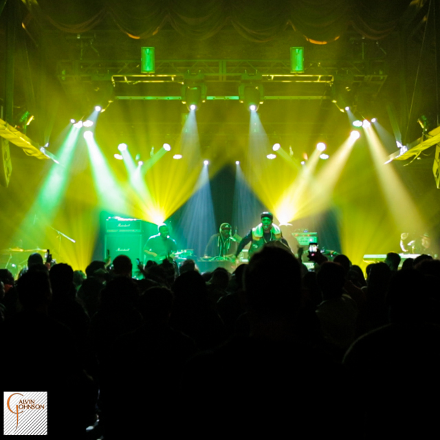 Hip Hop artist B.o.B performing in front of yellow and green beams of light at a concert with DJ Shawty Slim.