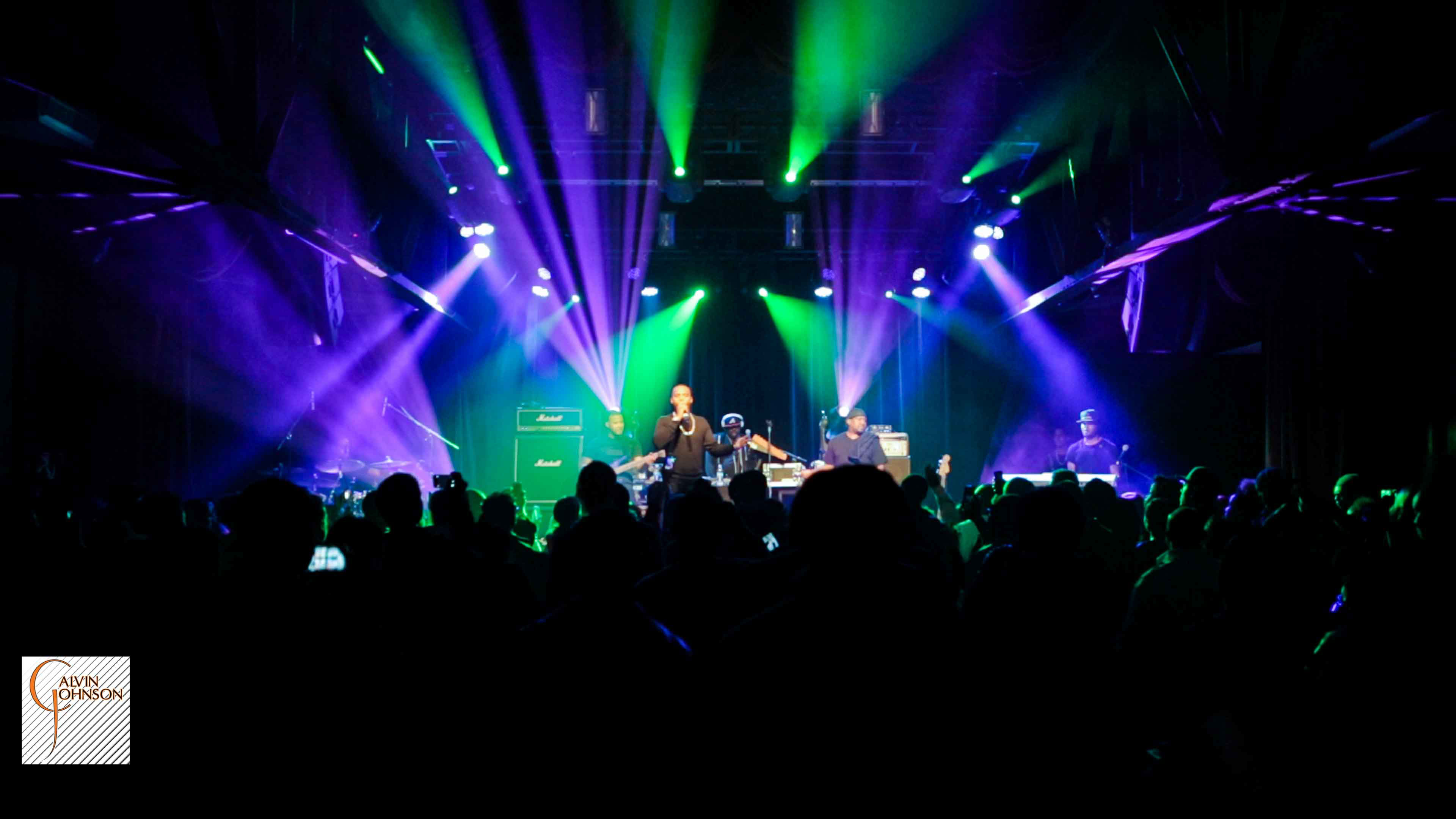 Hip Hop artist B.o.B performing in front of purple and green beams of light at a concert with DJ Shawty Slim.