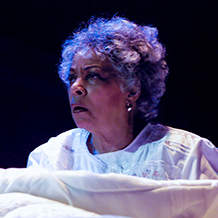 A woman sitting up in bed in the play "Flying Over Purgatory"