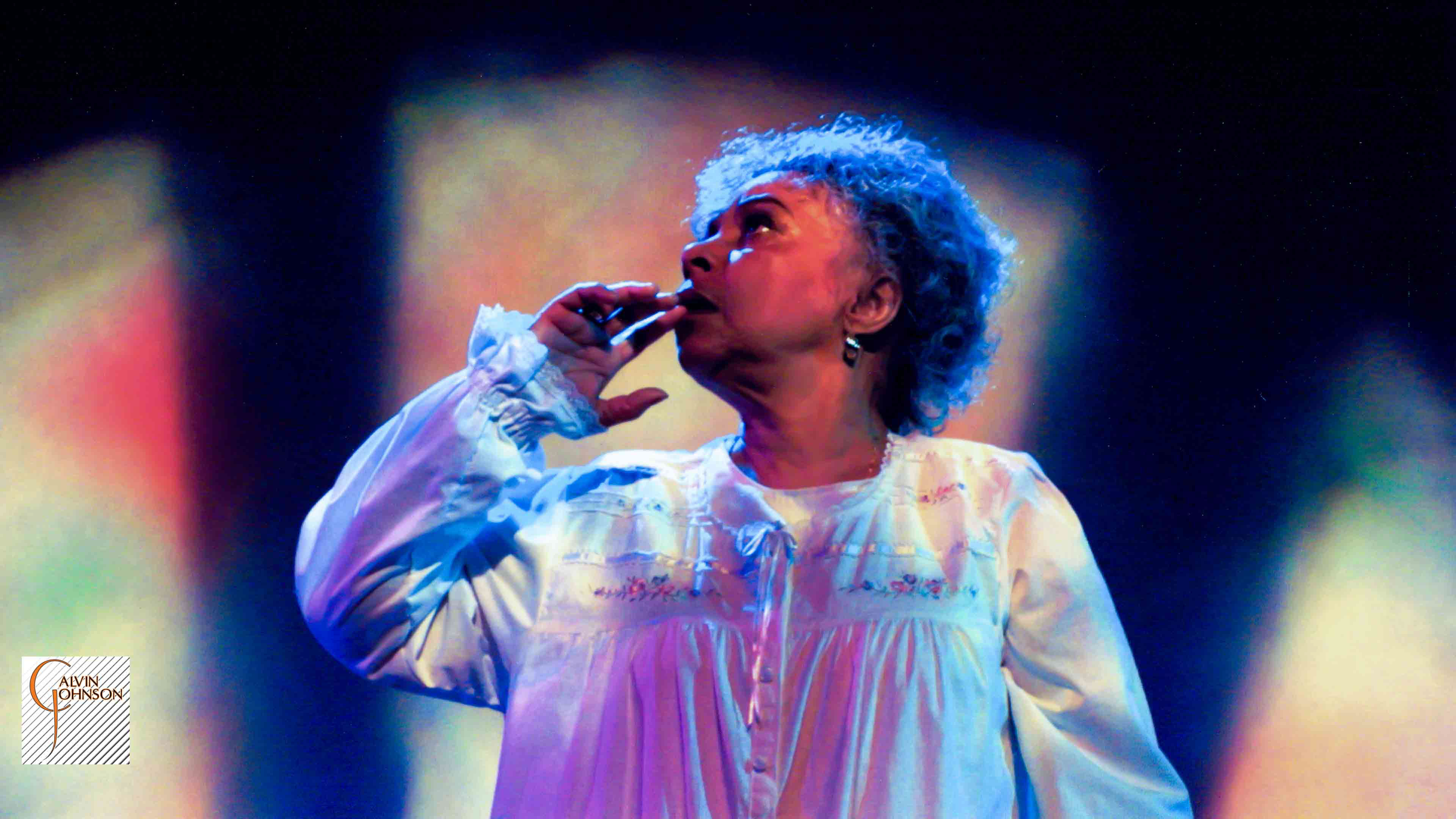 A woman looking off into the distance with fear up in bed in the play "Flying Over Purgatory"